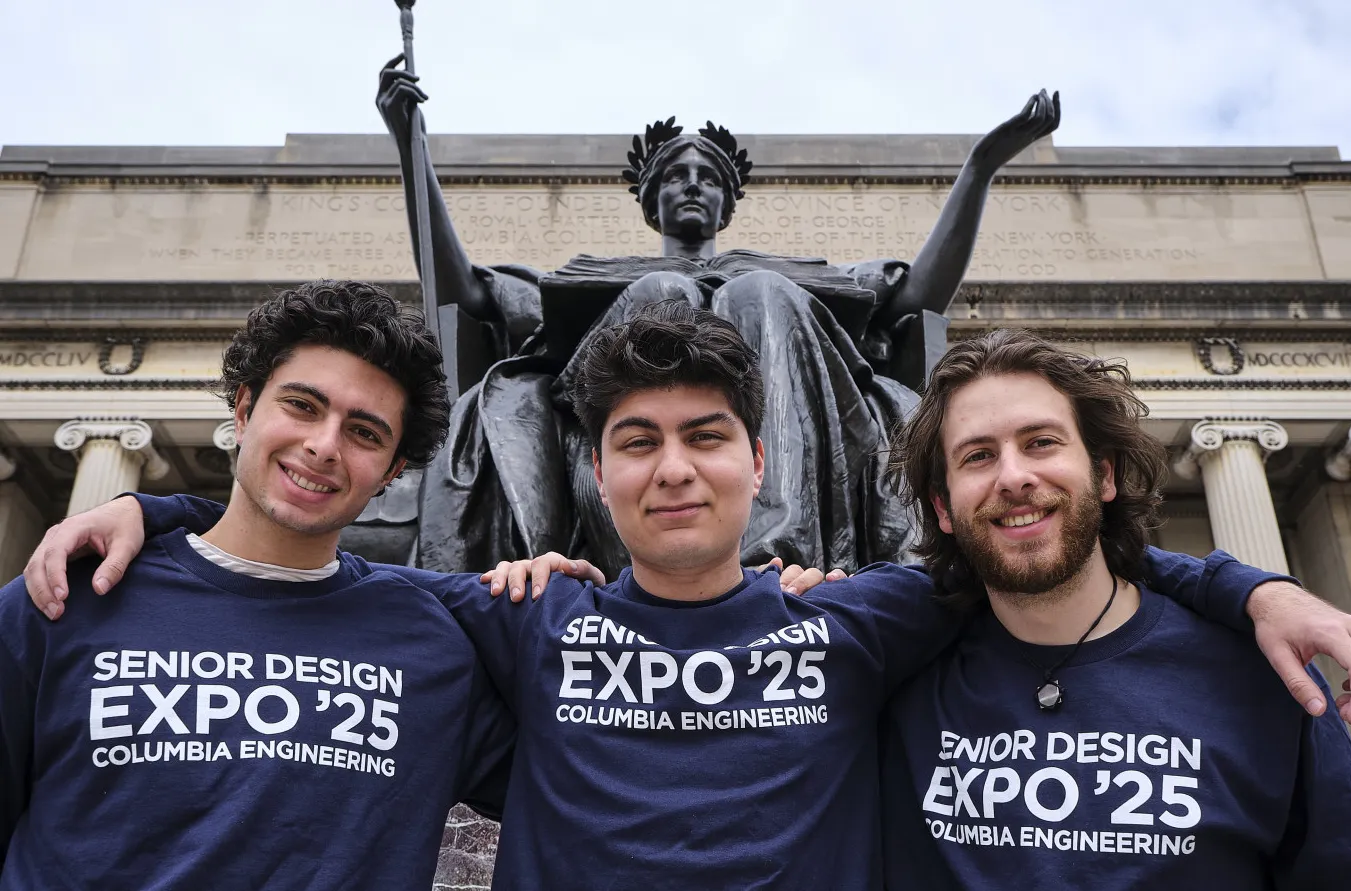 Three students stand with their arms over their shoulders in front of the Columbia alma mater statue 